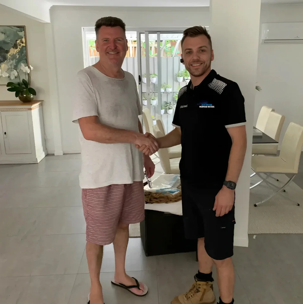 A customer and an electrician shaking hands, smiling in a modern living room.
